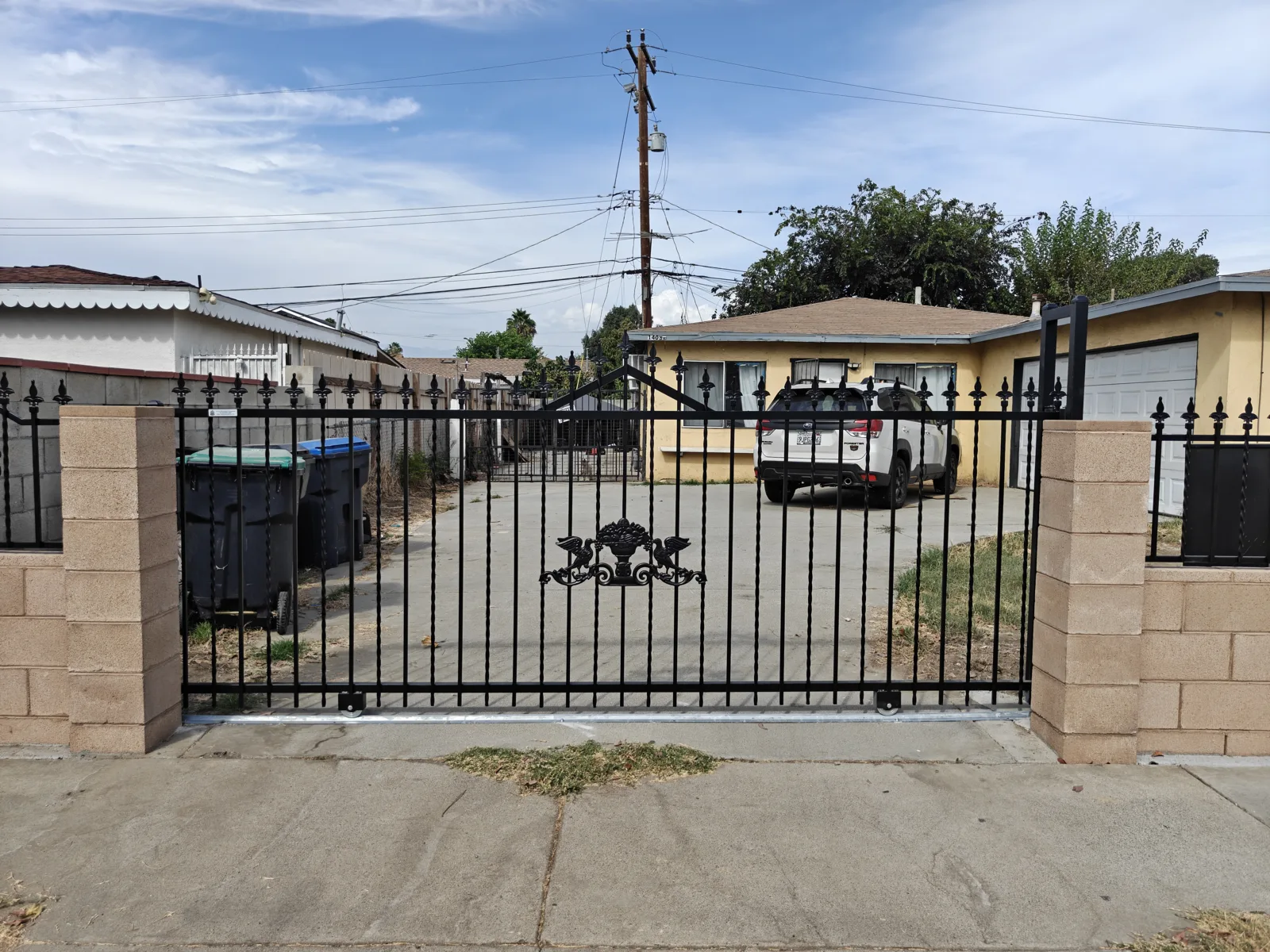 Sliding ornamental iron driveway gate with decorative center medallion between block pillars in Baldwin Park, CA by Apexguard Fence