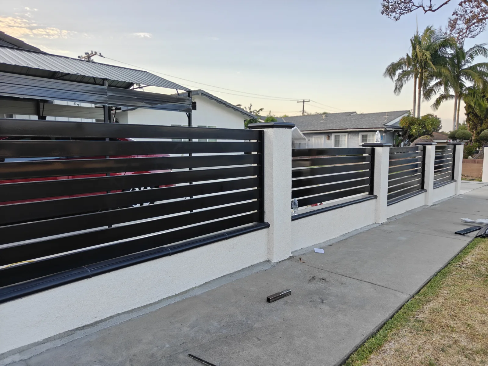 Long run of black horizontal slat fence on white stucco wall with palm trees — Apexguard Fence project in La Puente, CA