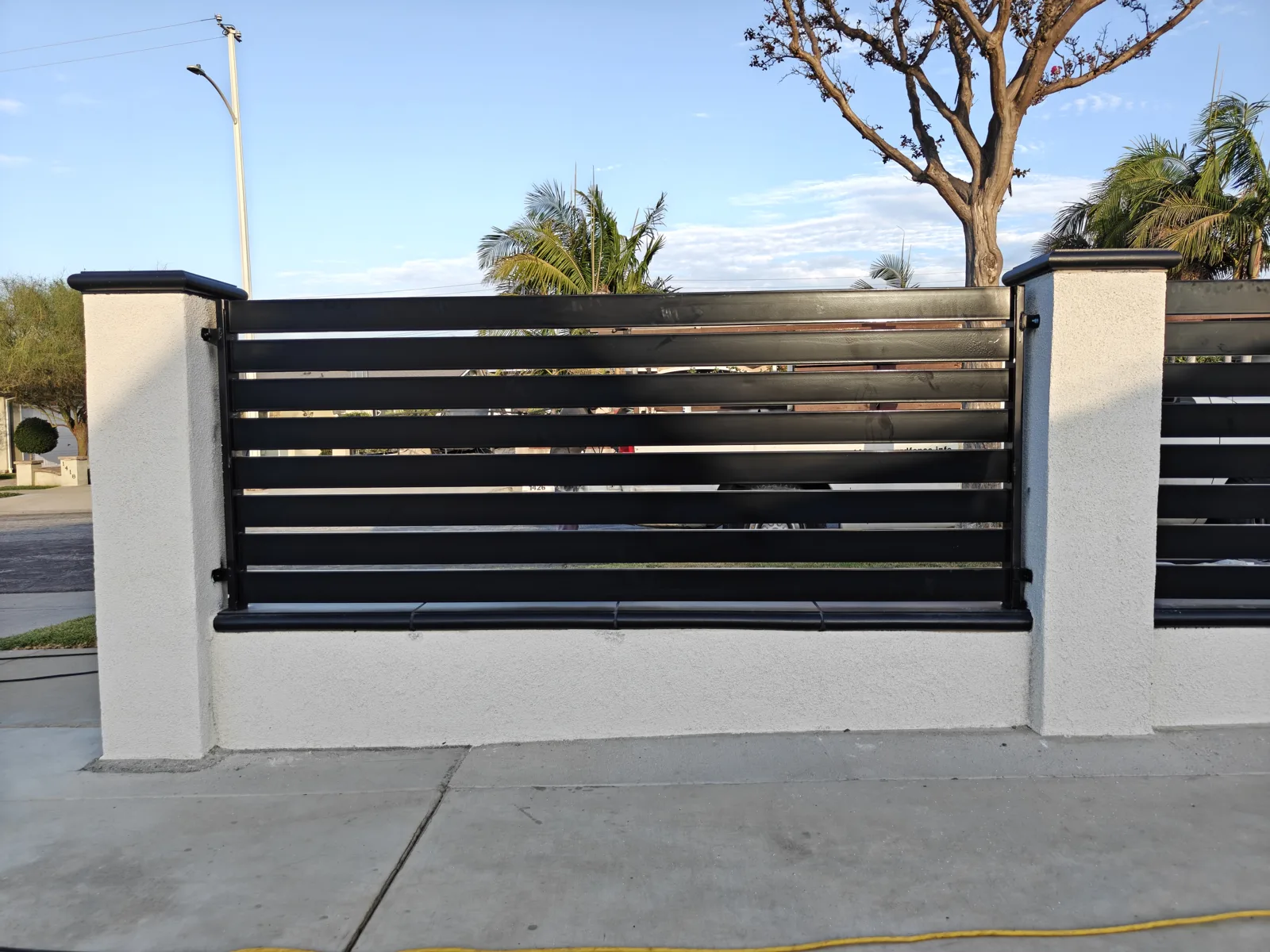 Black horizontal slat fence panel between white stucco CMU pilasters — a real Apexguard Fence project in La Puente, CA
