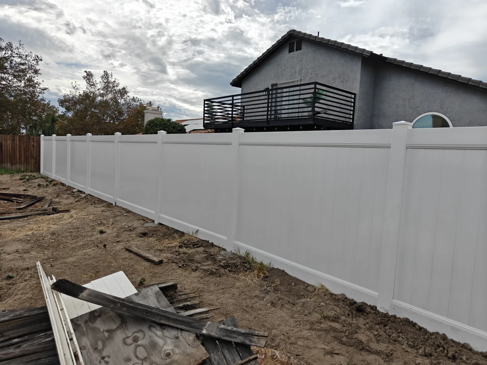 White vinyl privacy fence corner with the old torn-out wood fence boards on the ground — a real Apexguard Fence project in San Bernardino, CA