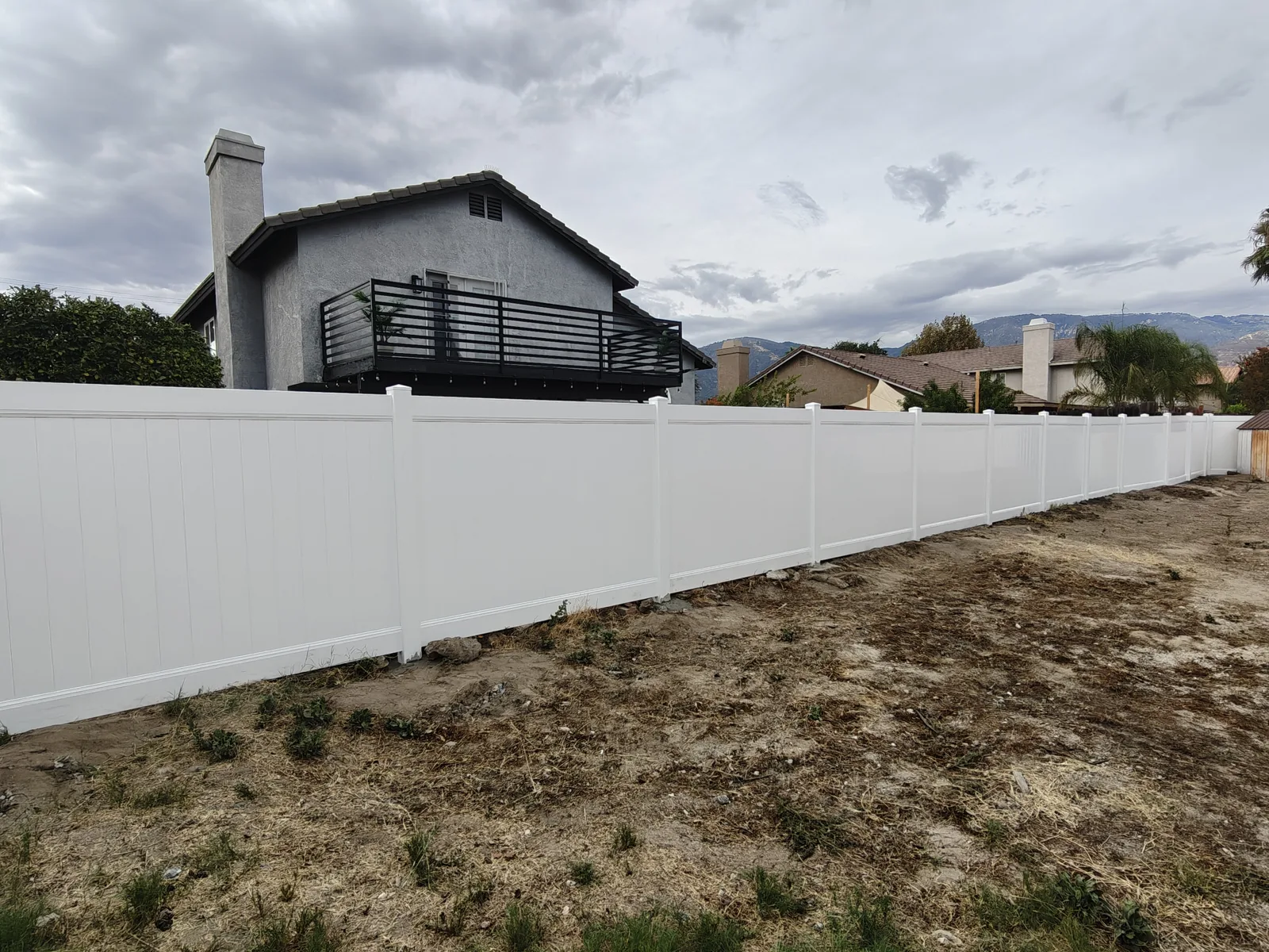 Long white vinyl privacy fence stepped along a sloped backyard — a real Apexguard Fence project in San Bernardino, CA
