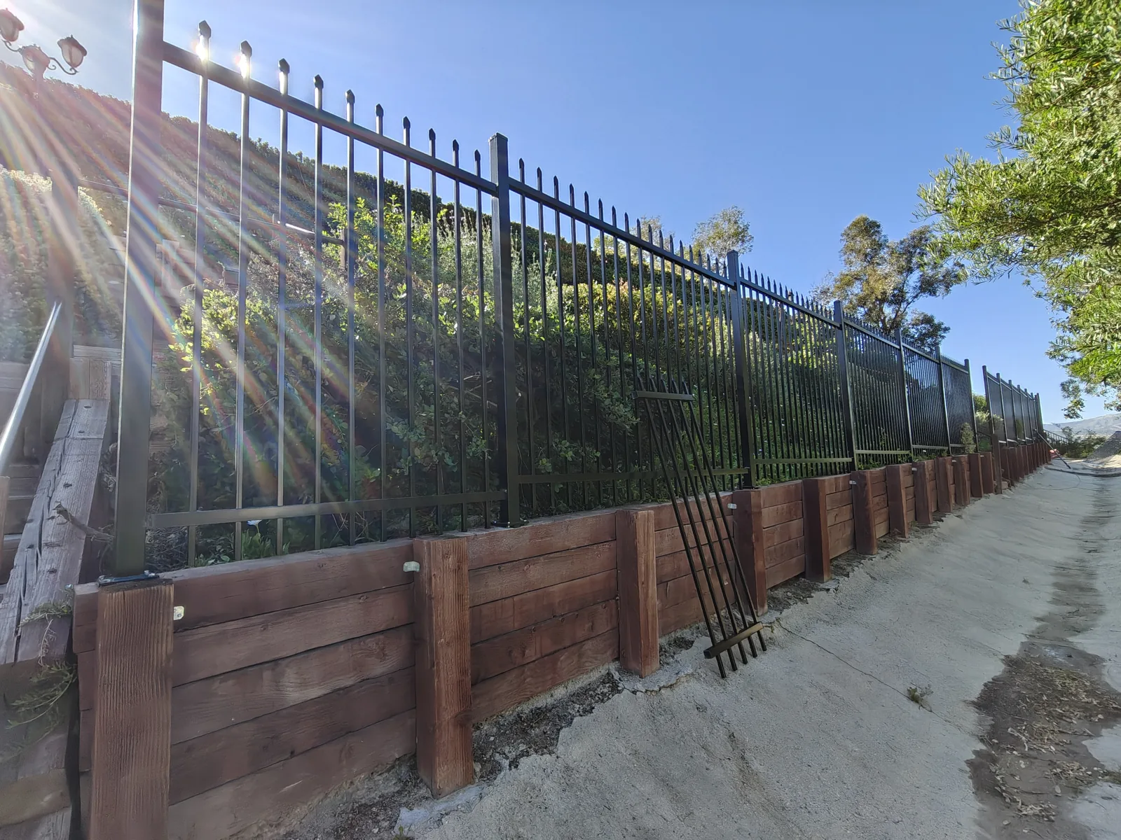 Long run of 6-foot black spear-top wrought iron fence along a hillside retaining wall in West Hills, CA