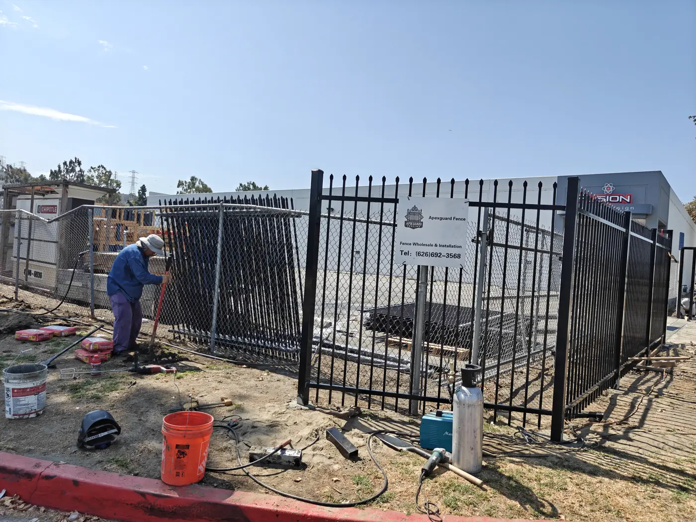 Welder joining 7 ft spike-top steel fence panels on site at a Whittier, CA commercial property
