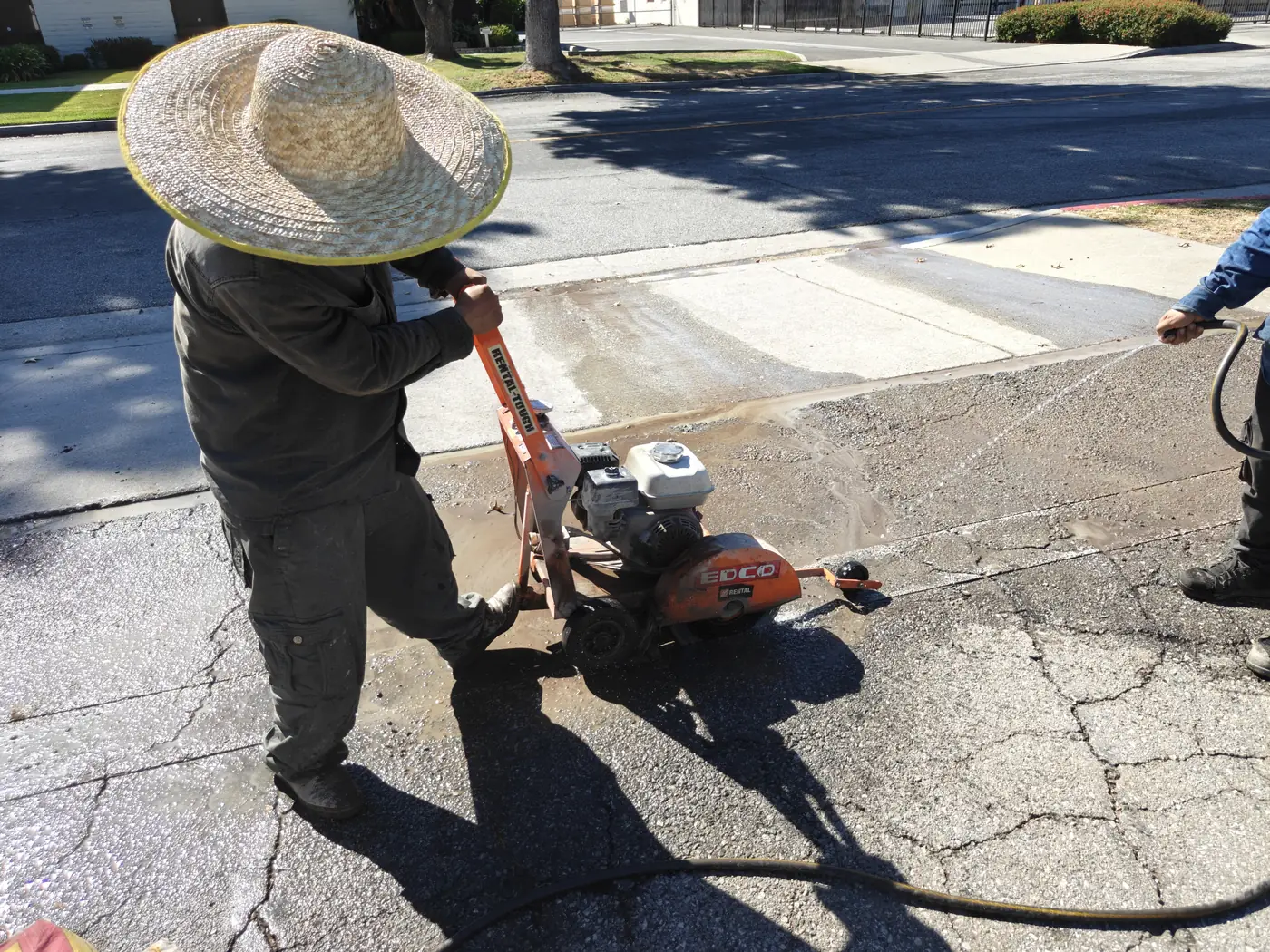 Crew saw-cutting asphalt with a walk-behind concrete saw to open the fence footing line at a Whittier, CA commercial yard