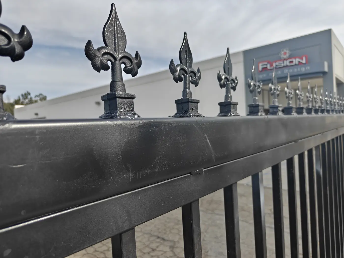 Close-up of cast fleur-de-lis finials on the top rail of a 7 ft commercial steel fence at the Fusion Sign & Design facility in Whittier, CA